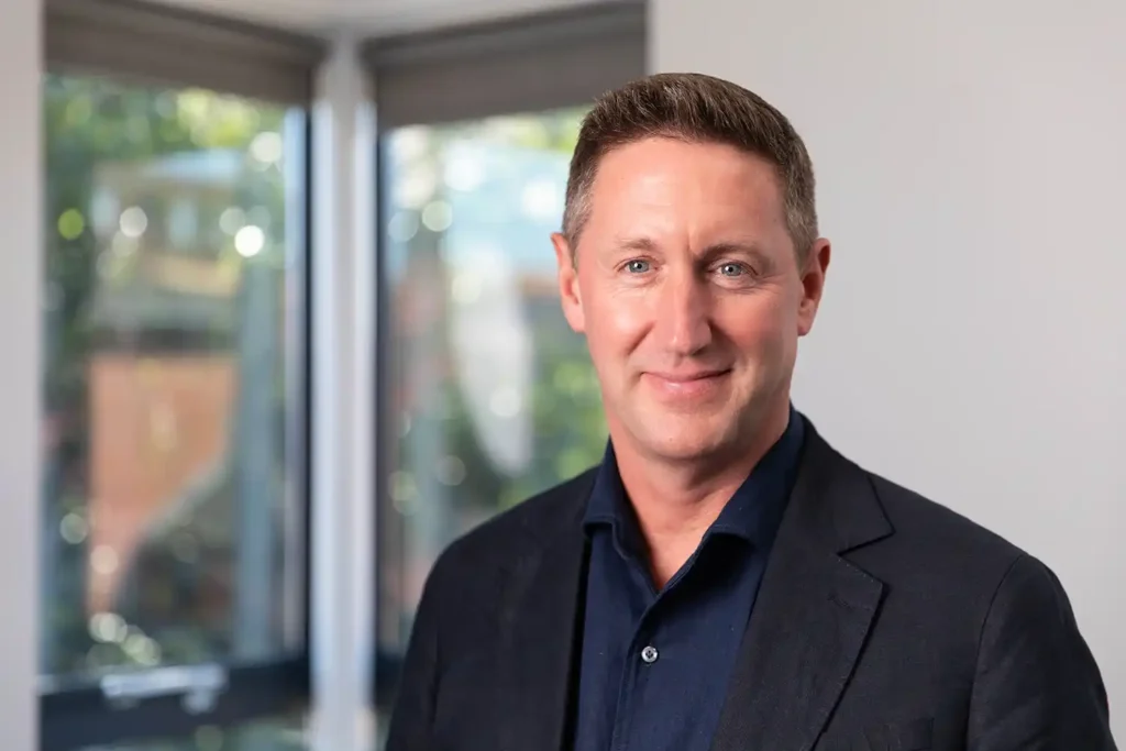 Commercial photograph of a Chief Executive Officer (CEO). Showing a business person positioned near a window with trees beyond.