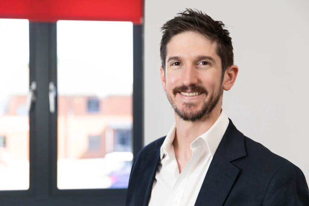 Headshot of a senior leader at an asset finance company. Showing a business person positioned near a window.