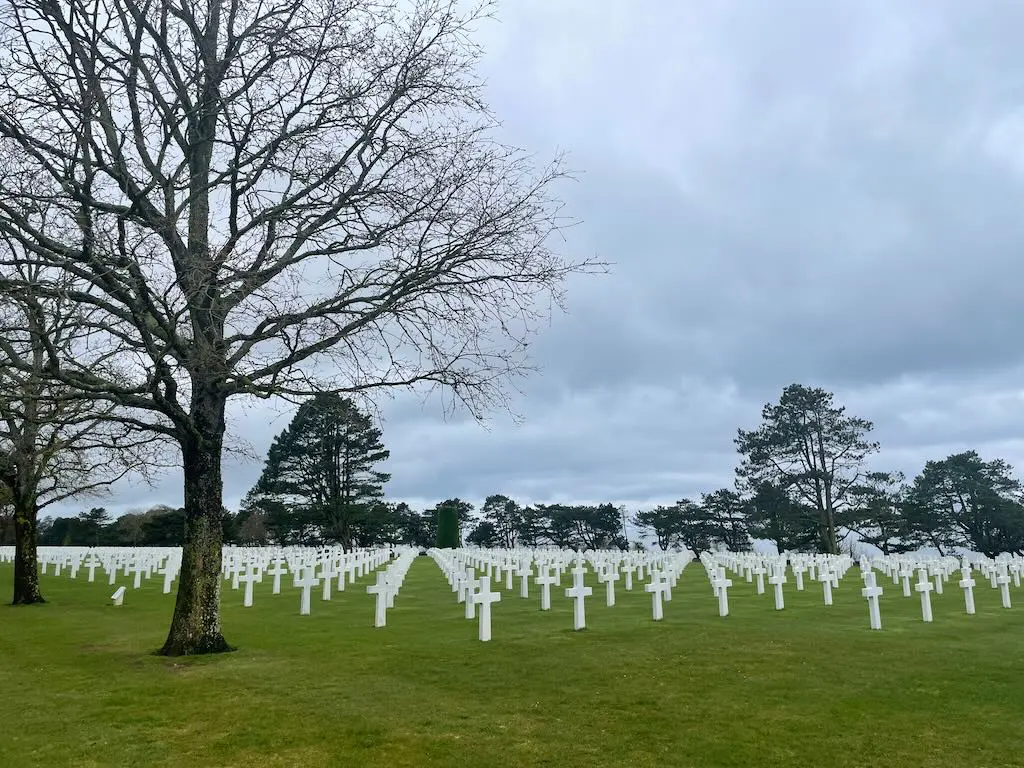 Rows of white crosses in a military cemetery stretching across green grass beneath grey clouds.