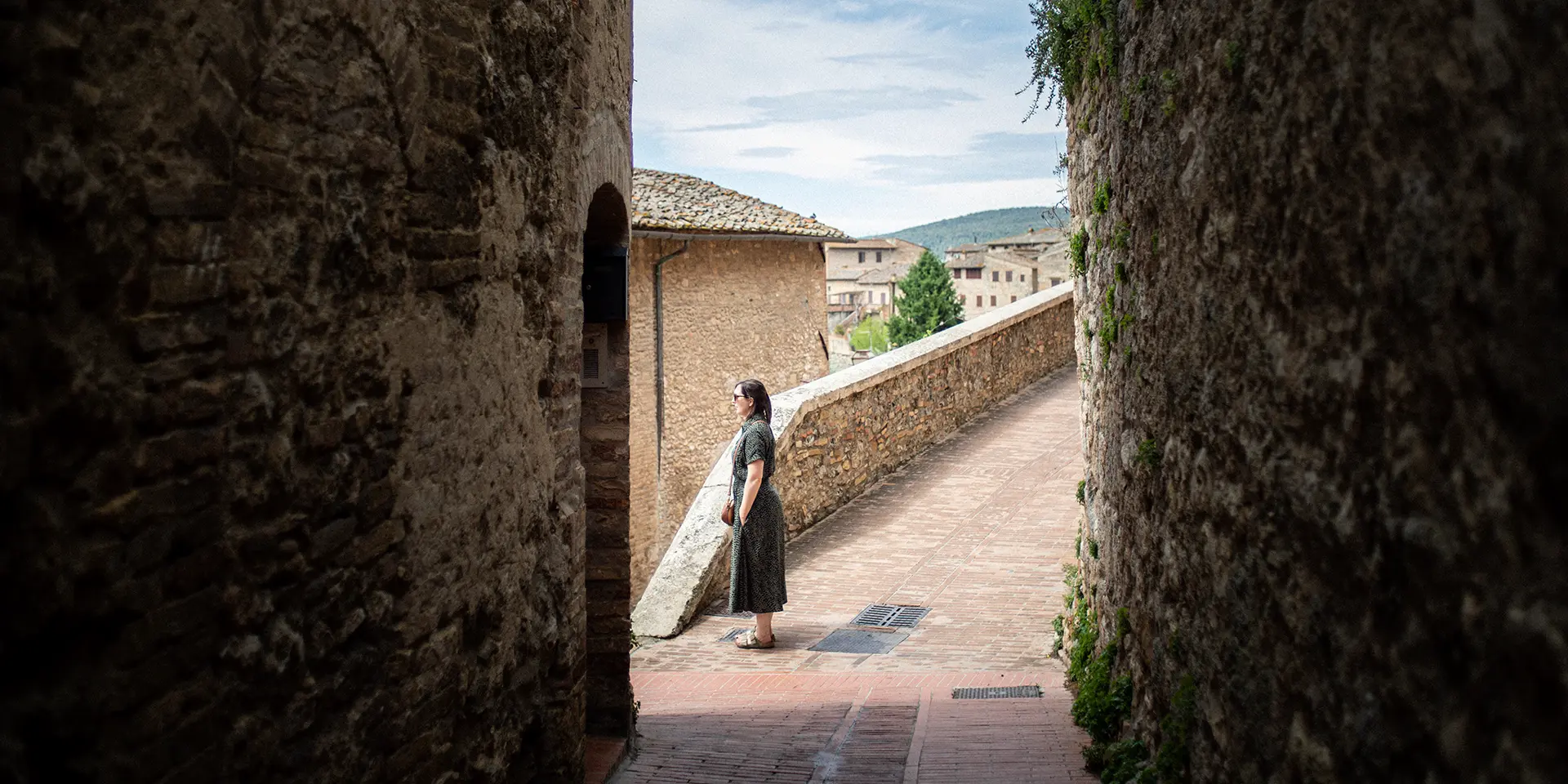 Photograph of a woman standing in a town in Italy looking out at the landscape beyond.