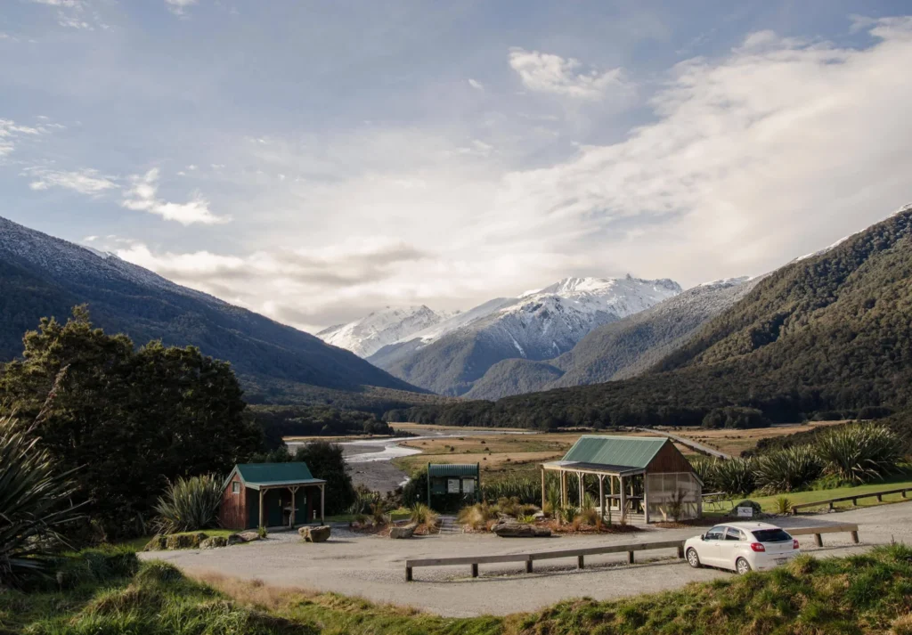 Photograph of a mountain range in New Zealand with buildings and a car in the foreground.