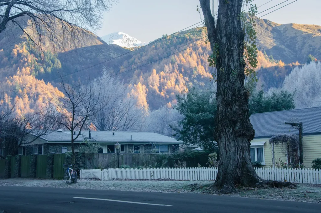 Single-storey house behind a white fence in a frosty mountain village.